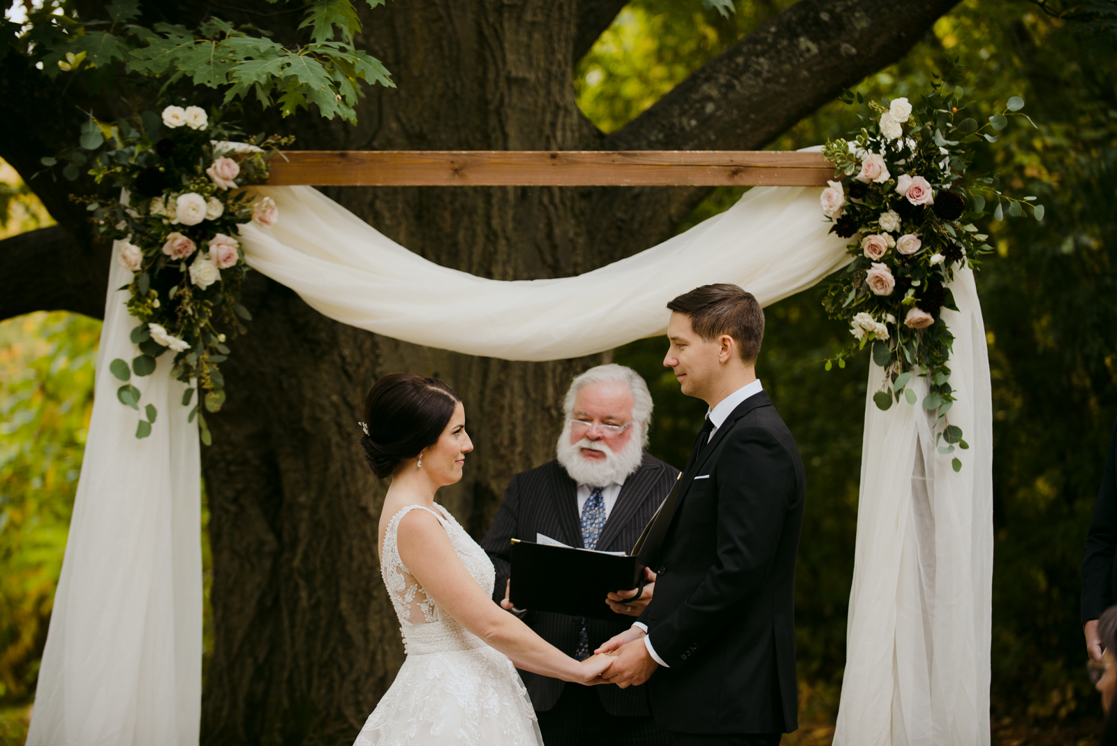 bride and groom holding hands underneath the wooden wedding arch during outdoor ceremony