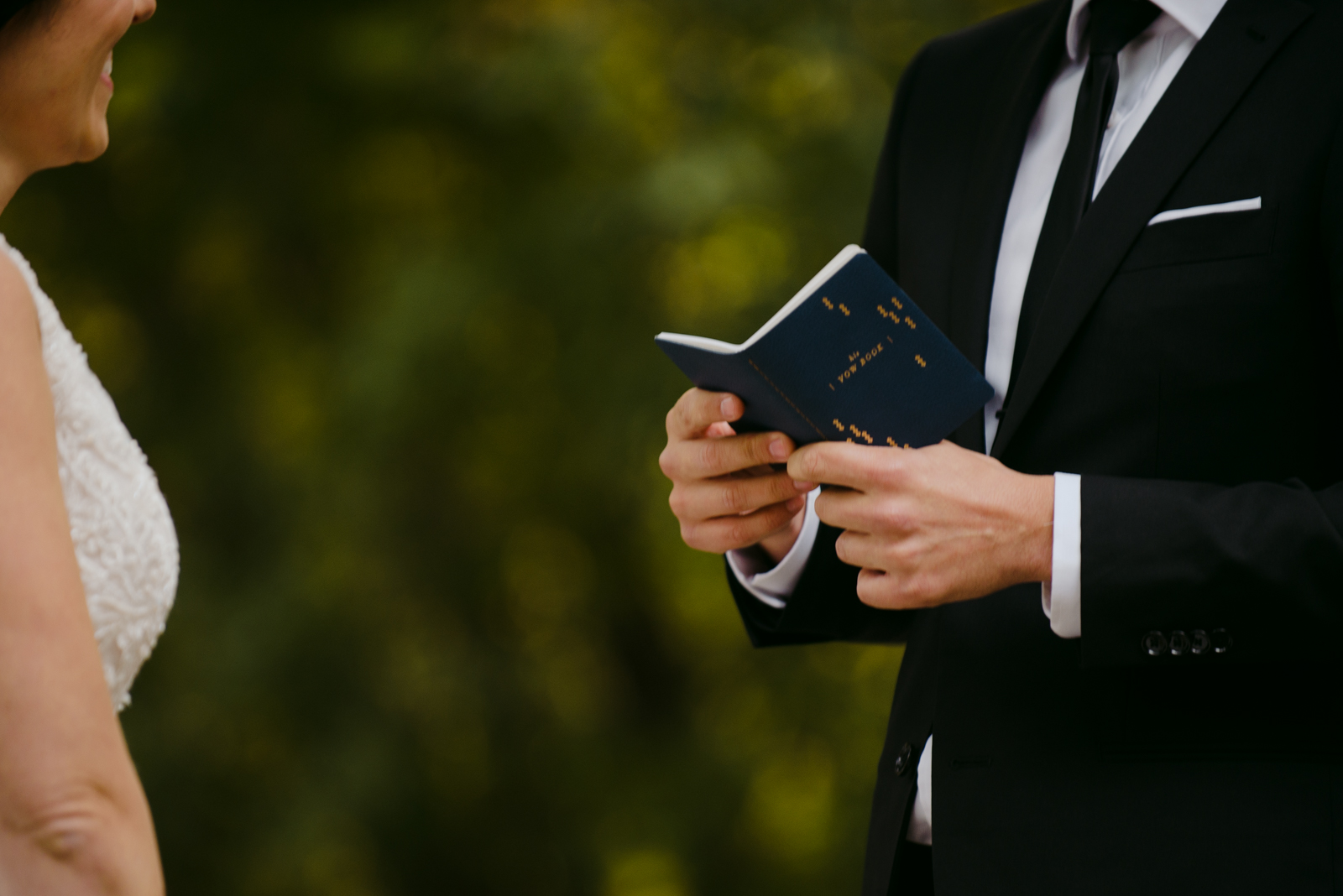 groom holding his vow book during outdoor wedding ceremony