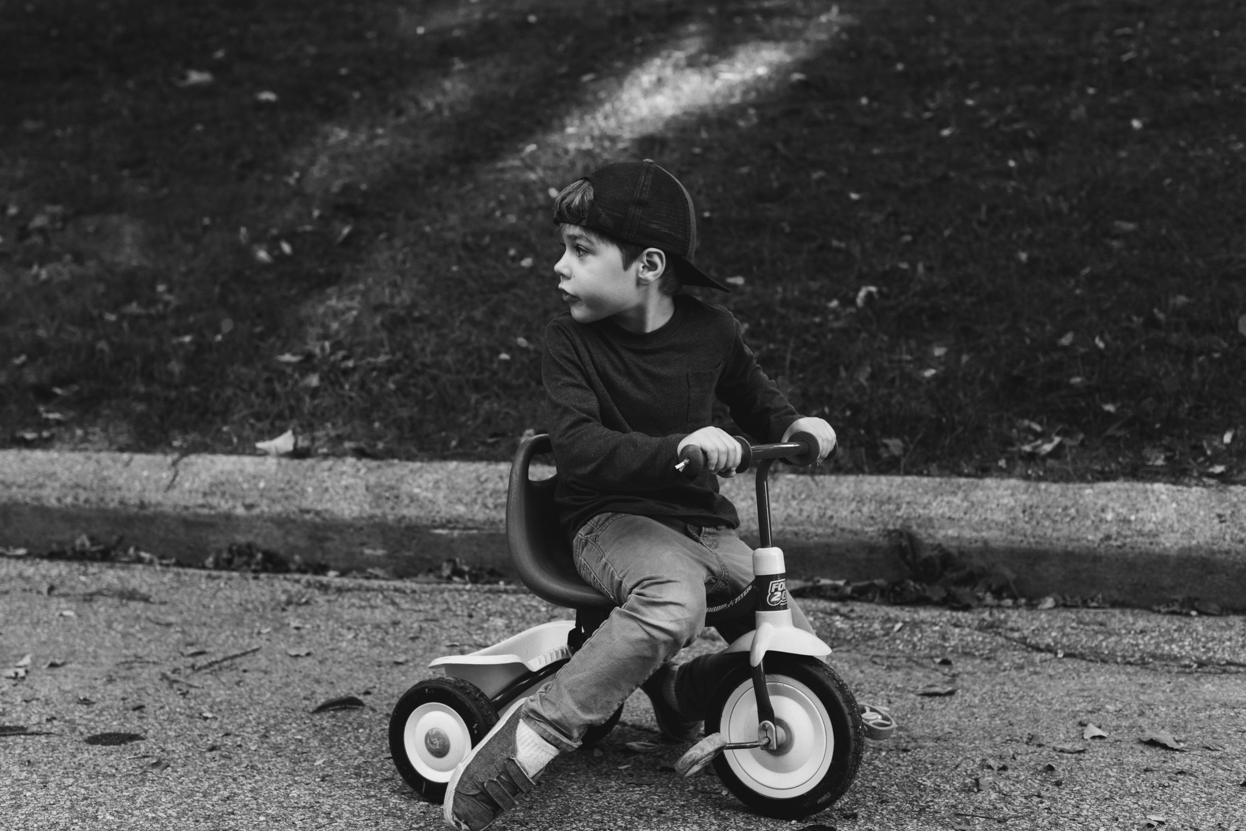 four year old boy on tricycle with backwards baseball hat