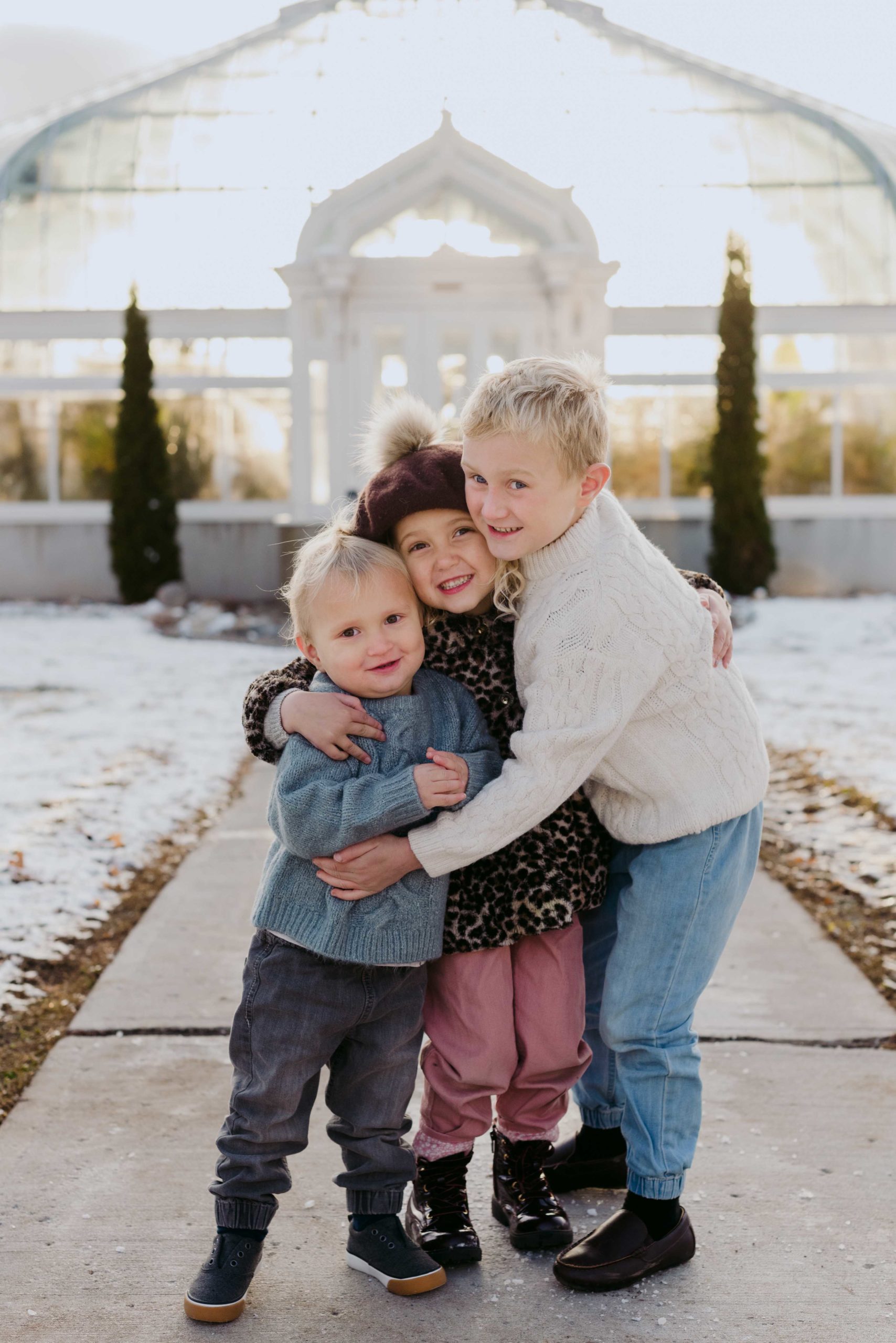 siblings hugging in front of experimental farm greenhouse in winter