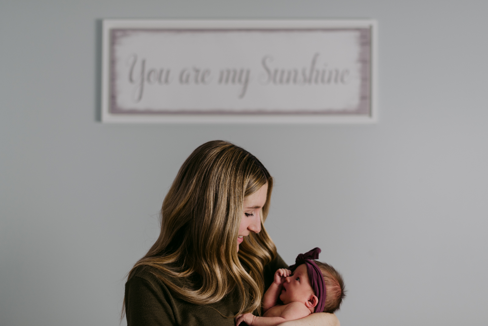 mom and baby girl with bow and sign that says "you are my sunshine"