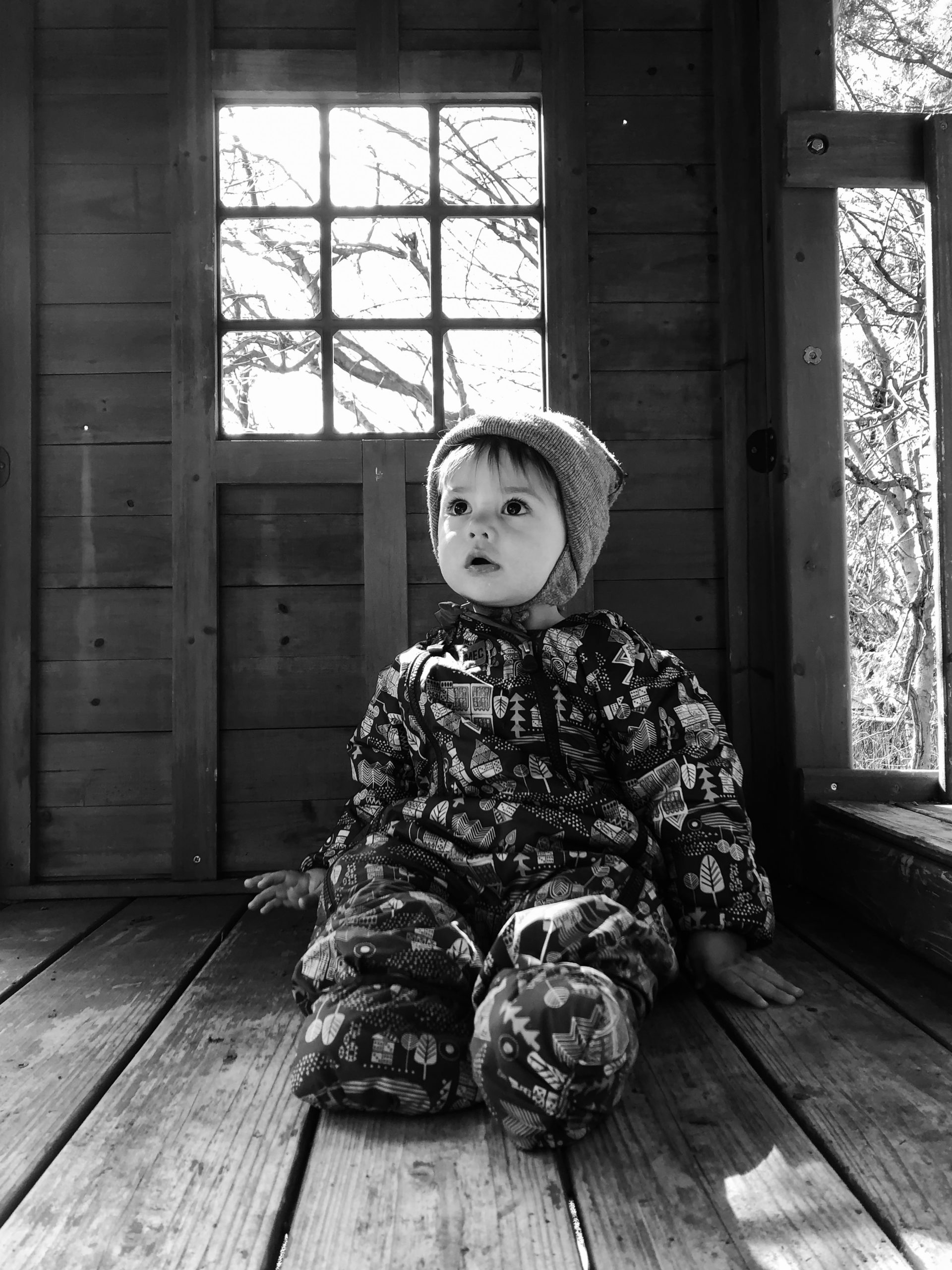 toddler in a snowsuit sitting in a treehouse