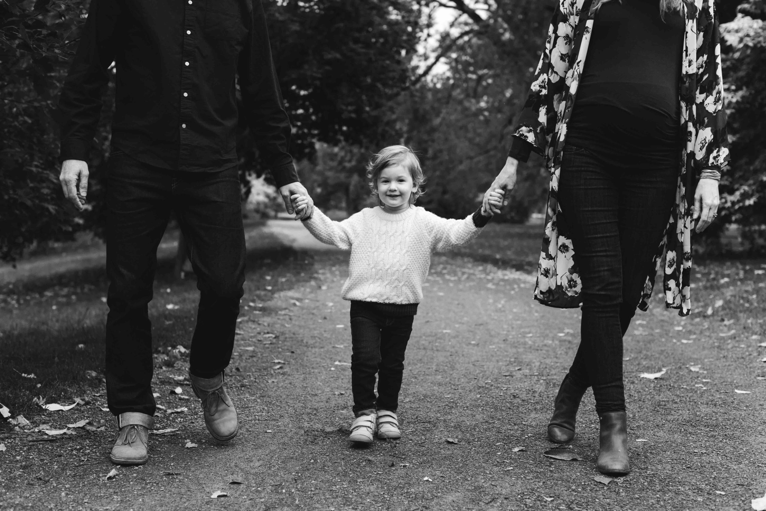 toddler holding his mom and dad's hands walking down a stone path