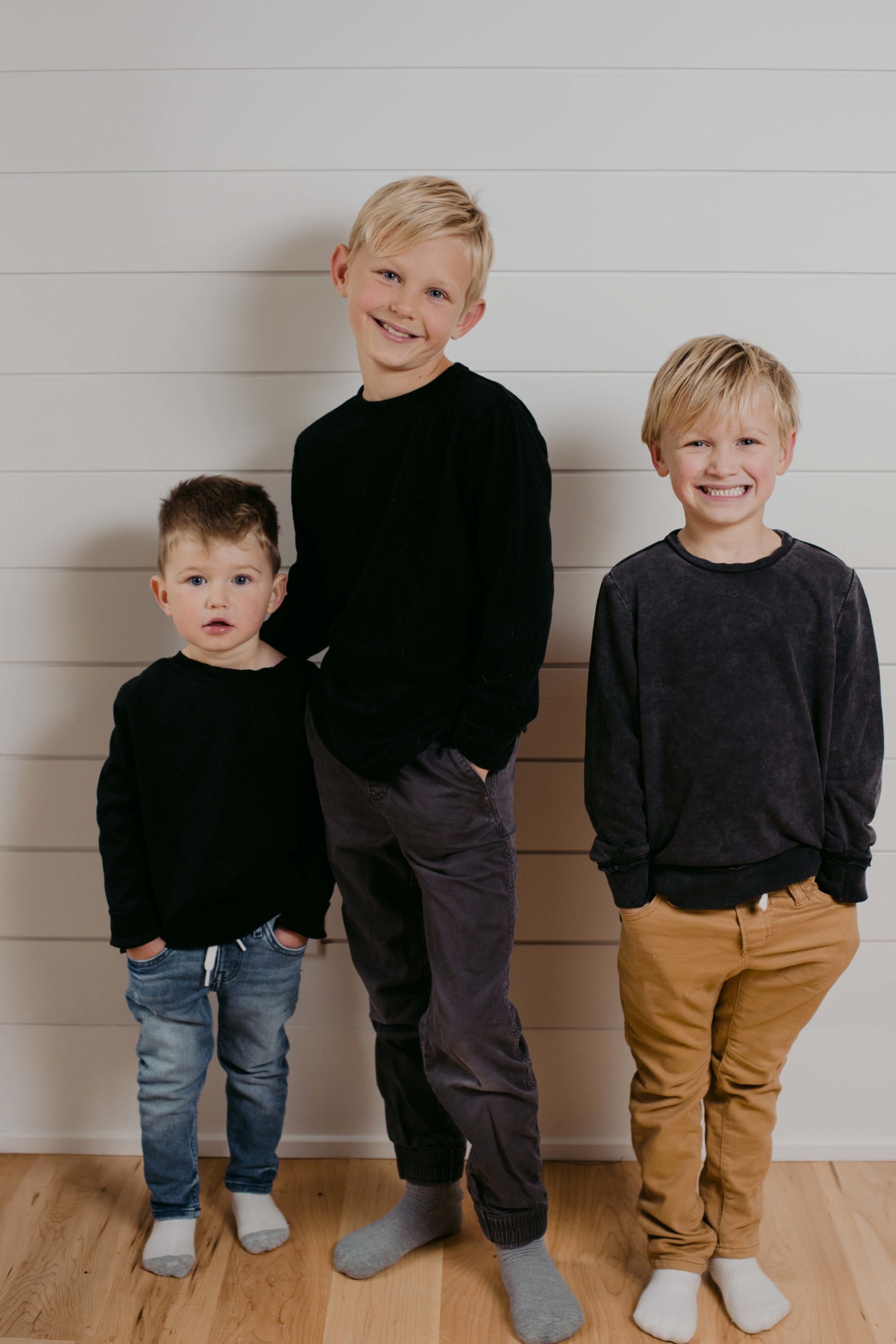 Three brothers standing against white wall smiling for the camera