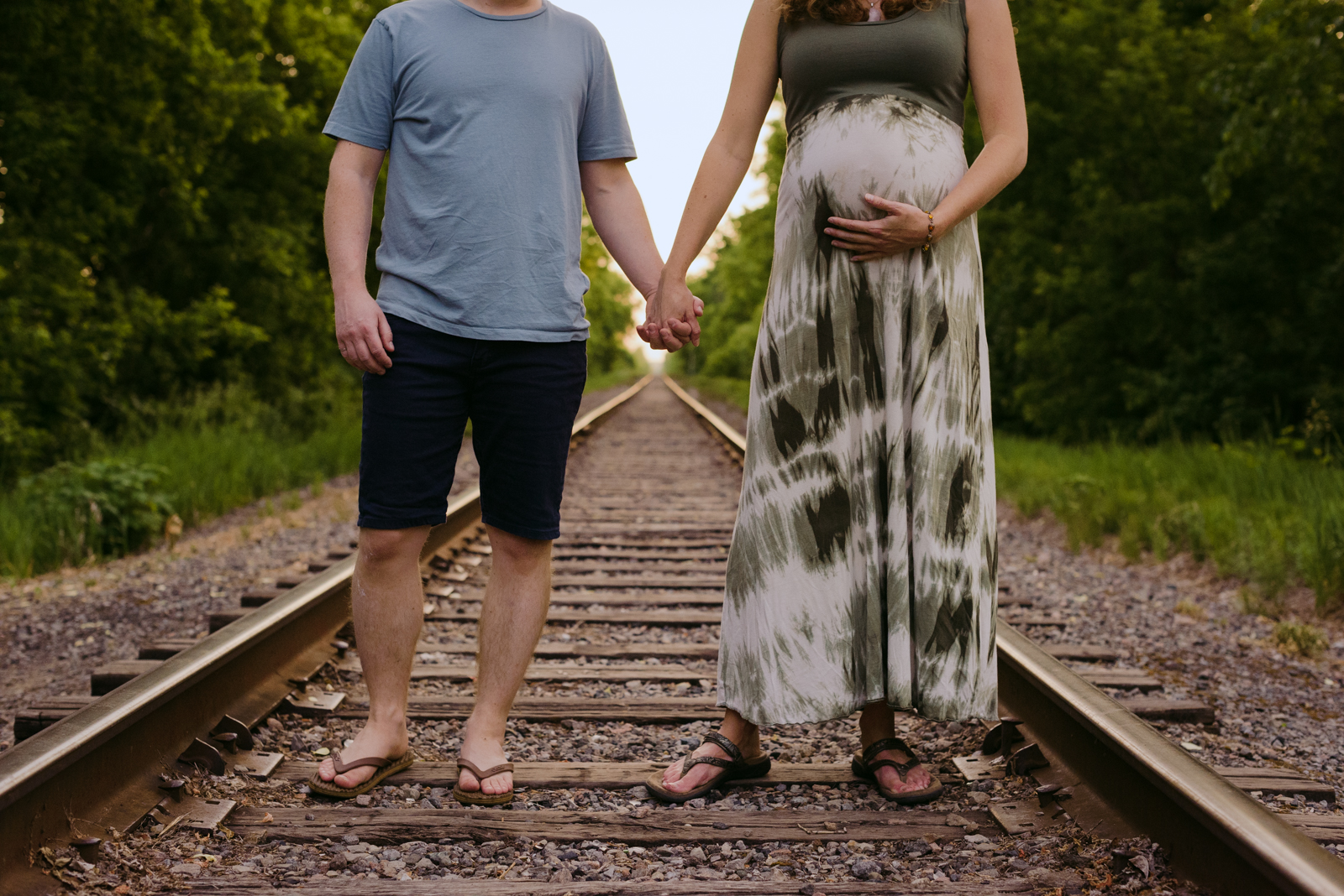 expecting parents holding hands on train tracks at sunset