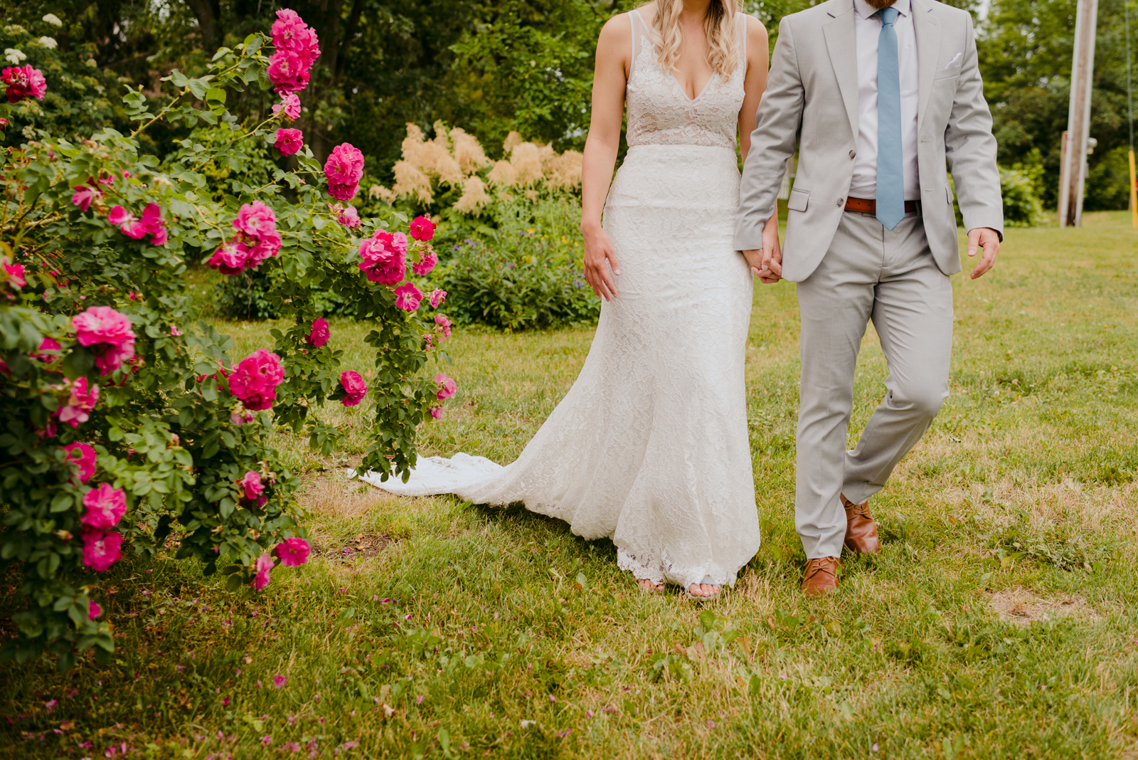 bride and groom walking through the garden of pink roses at Strathmere