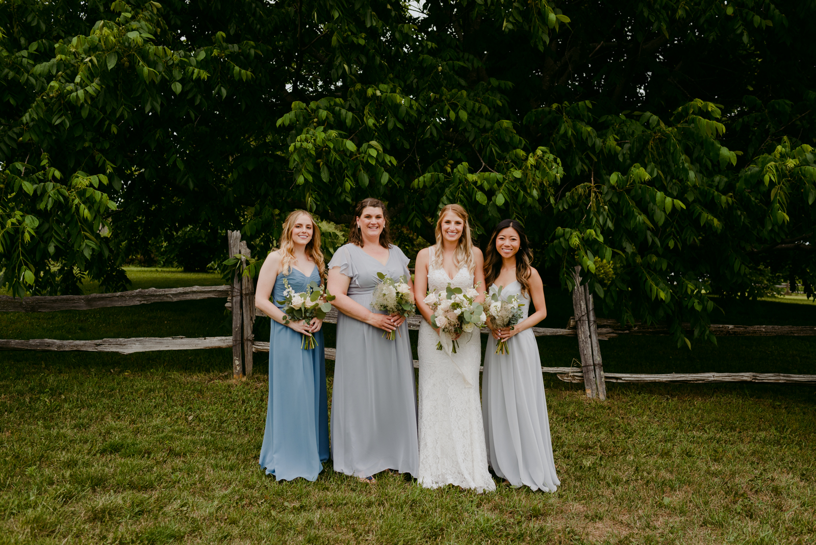 bride and bridesmaids in blue and grey by wooden fence