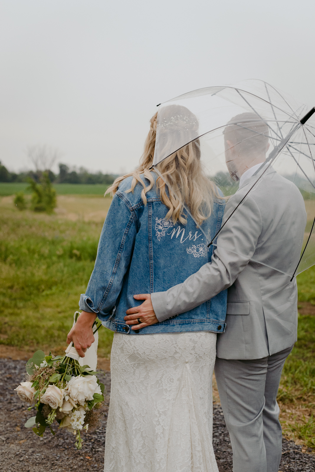 bride wearing Mrs. jean jacket under an umbrella in a field at Strathmere