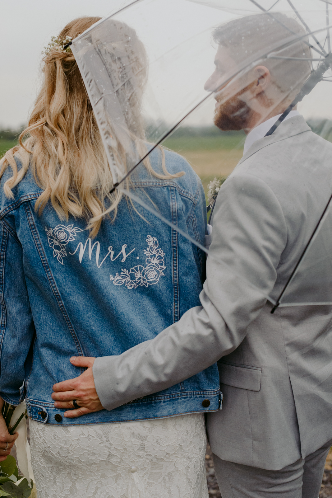 bride wearing Mrs. jean jacket under an umbrella in a field at Strathmere