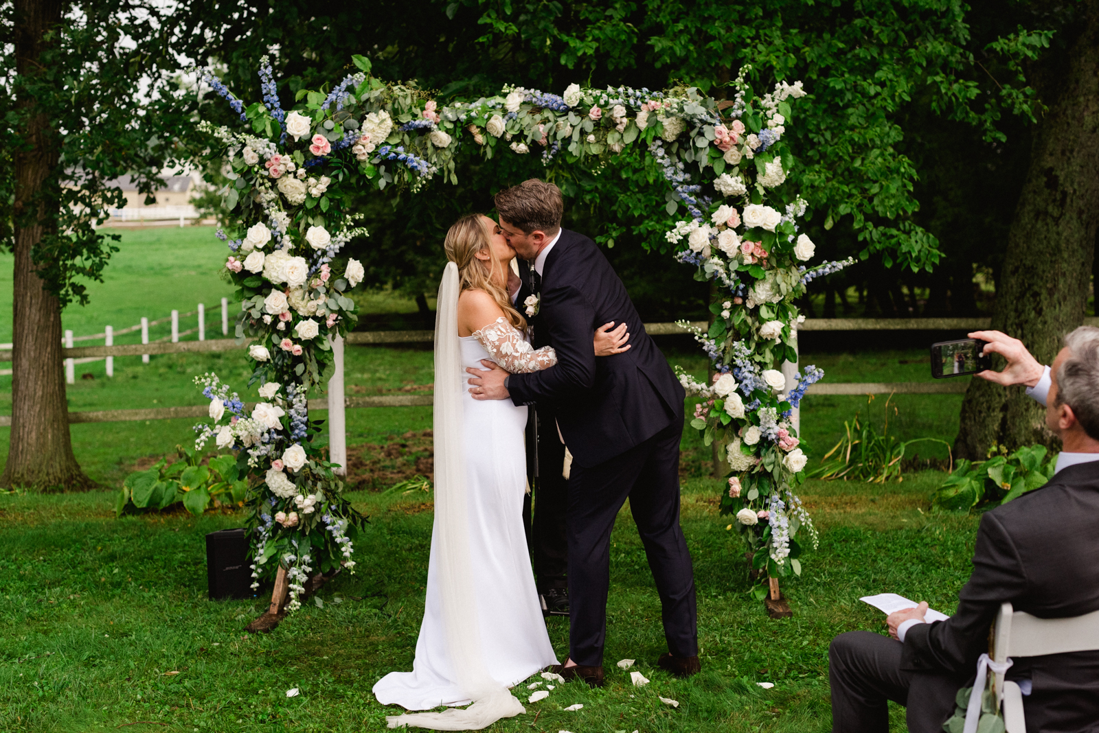 bride and groom first kiss under floral arch