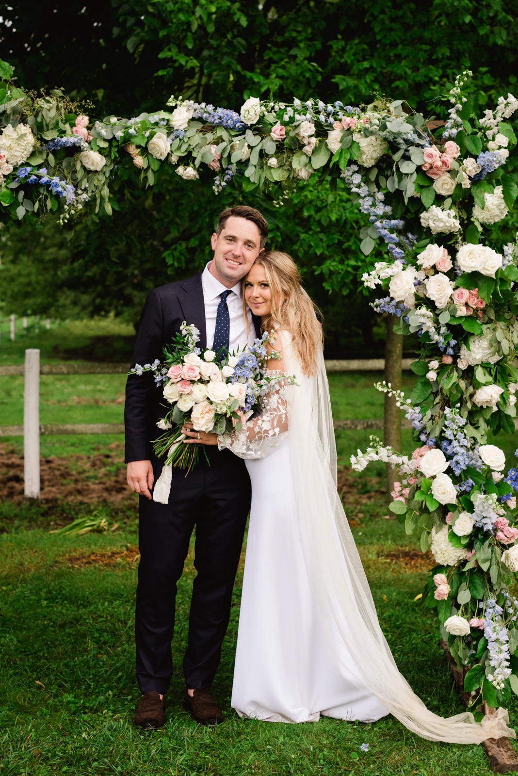 bride and groom standing under floral wedding arch