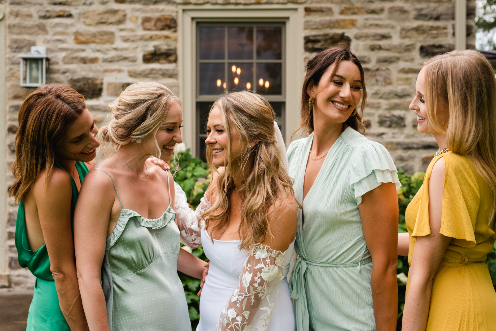bride and bridesmaids laughing in front of old stone farmhouse