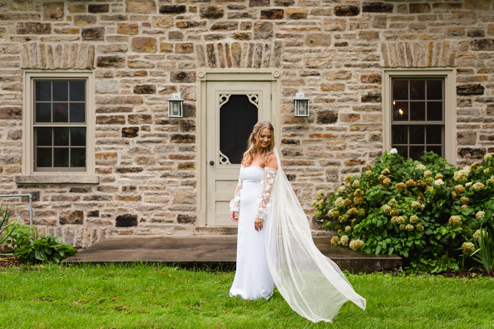 bride's cathedral veil blowing in the wind in front of old stone farmhouse