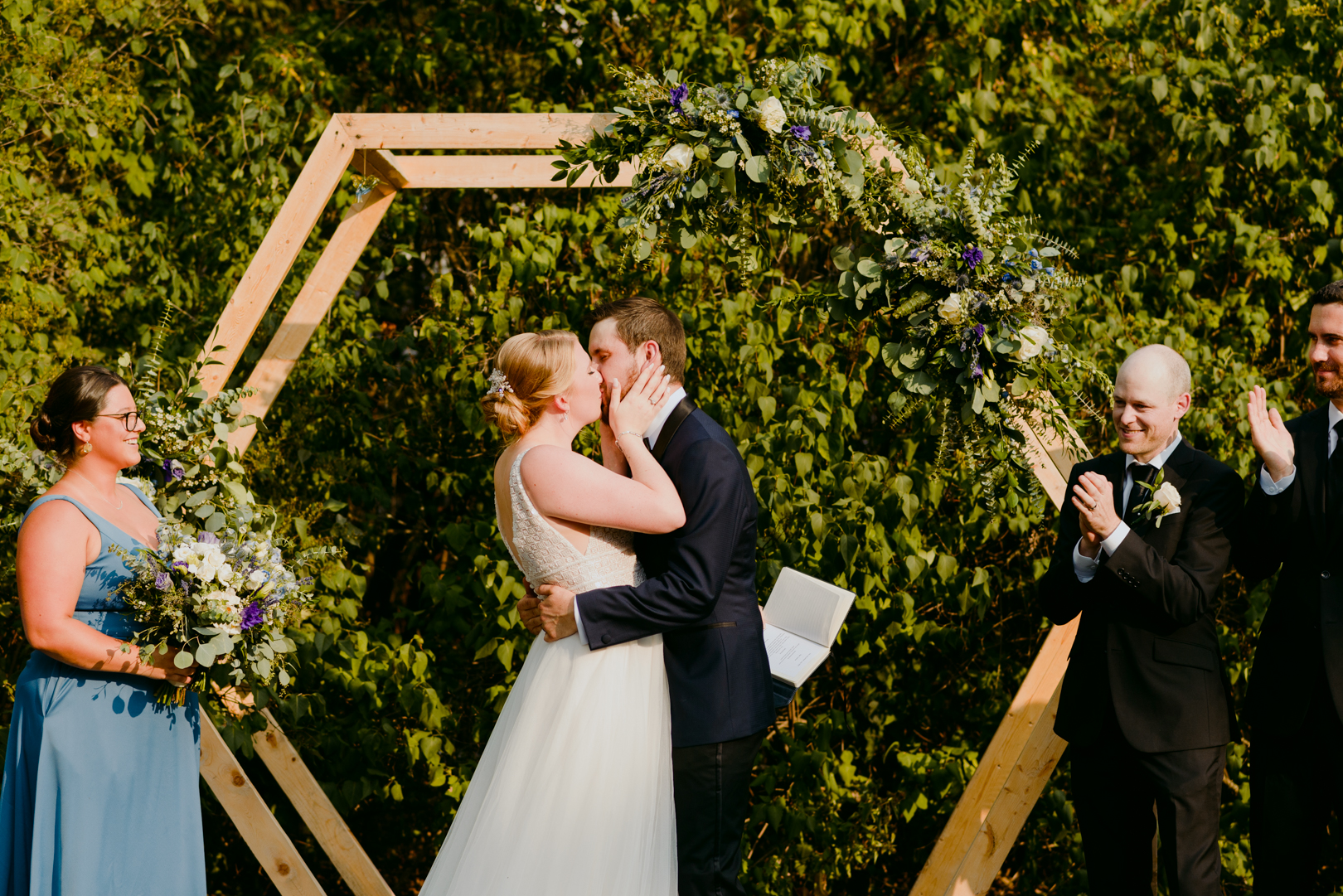 bride and groom first kiss in front of wooden hexagon during outdoor wedding ceremony