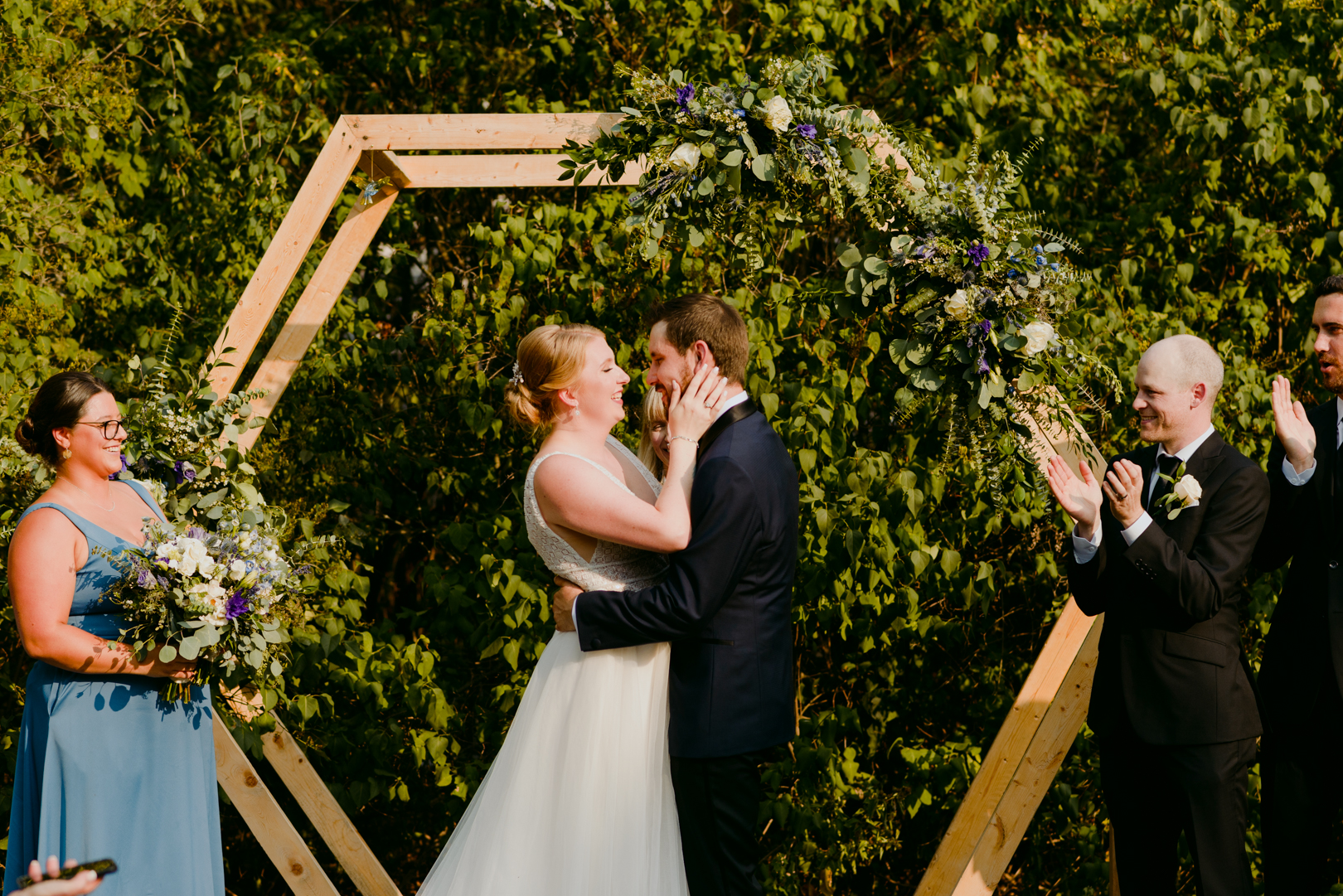 bride and groom first kiss in front of wooden hexagon during outdoor wedding ceremony