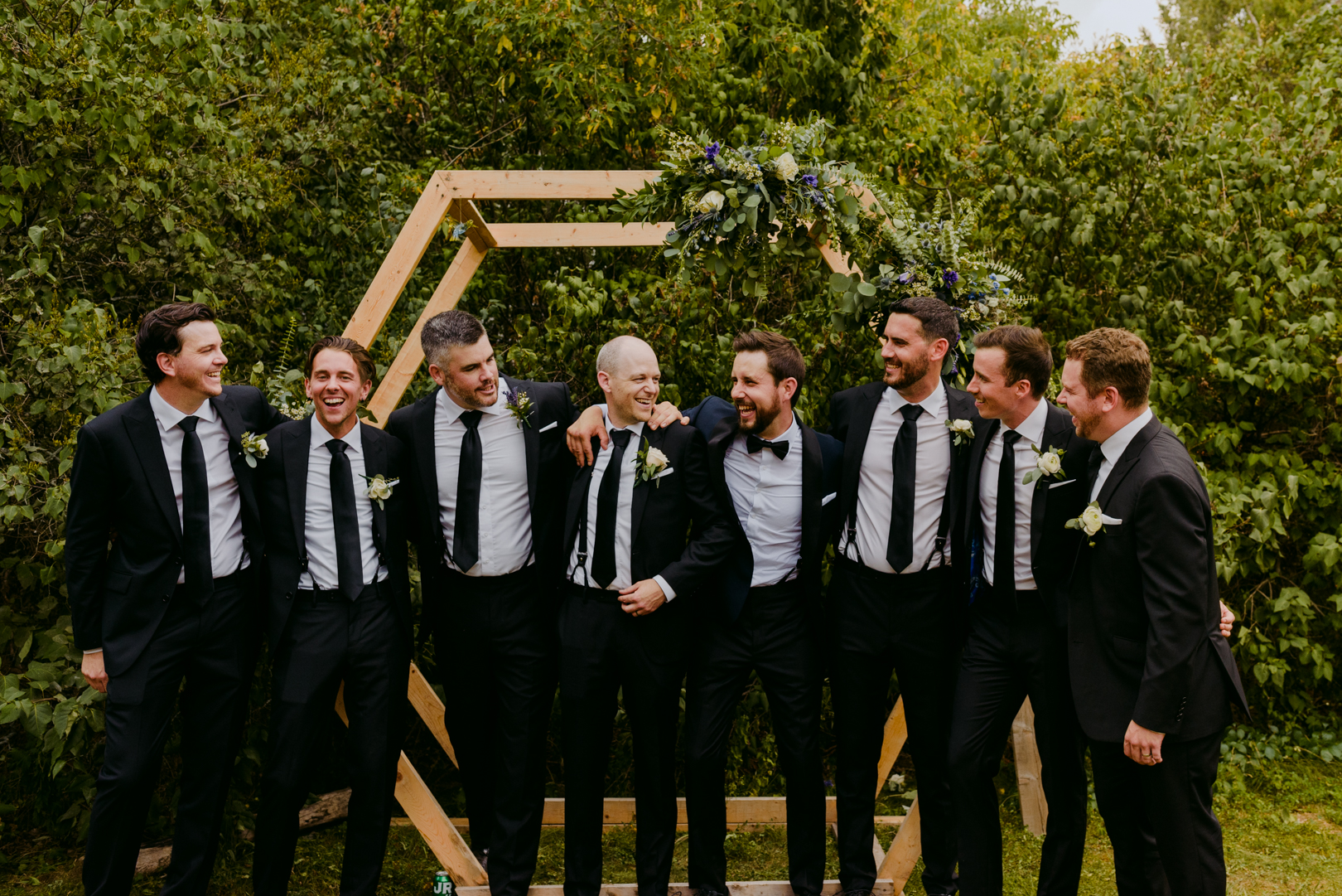 groom and groomsmen laughing together in front of wooden hexagon