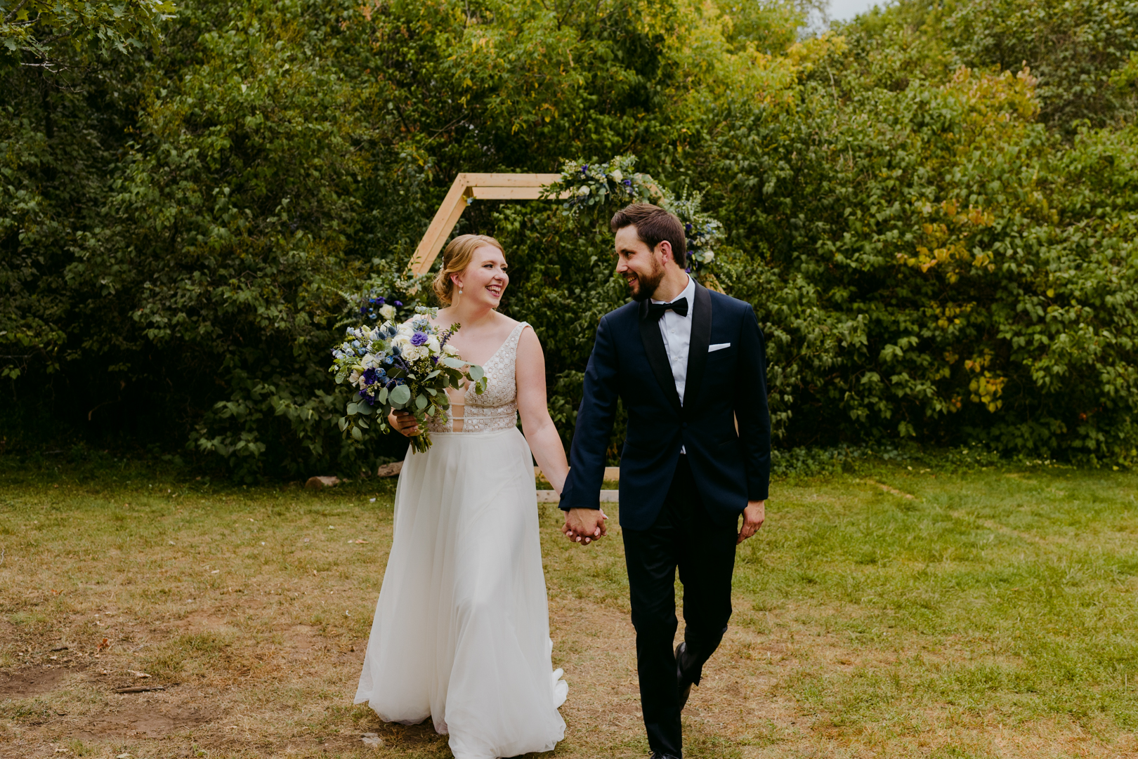 bride and groom holding hands walking in front of wooden hexagon