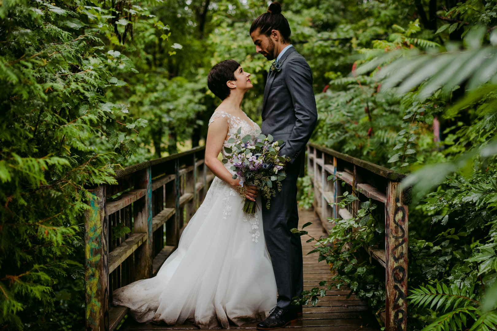 bride and groom standing on a wooden bridge surrounded by trees