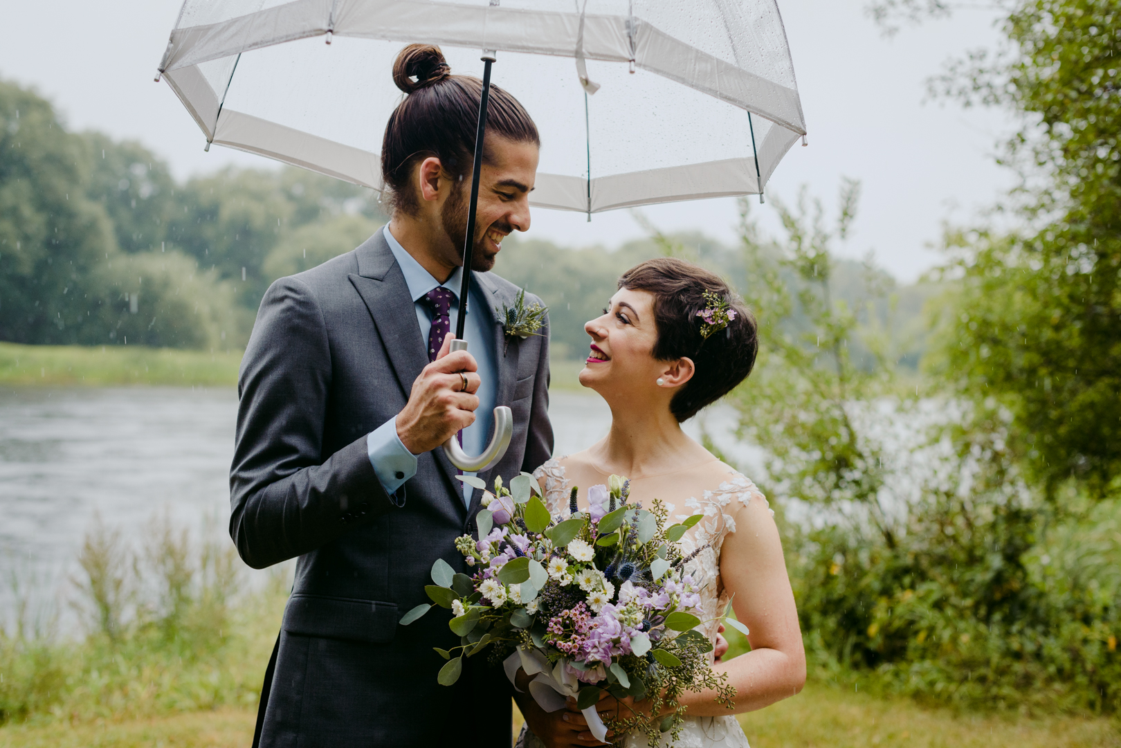 bride and groom holding an umbrella smiling at each other