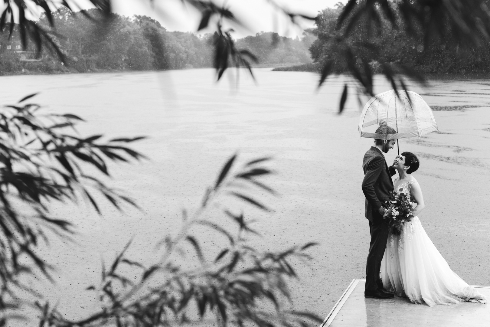 bride and groom standing on a dock by the water with umbrellas