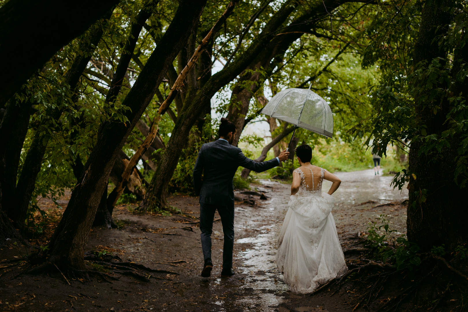 bride and groom walking under tree canopy in the rain