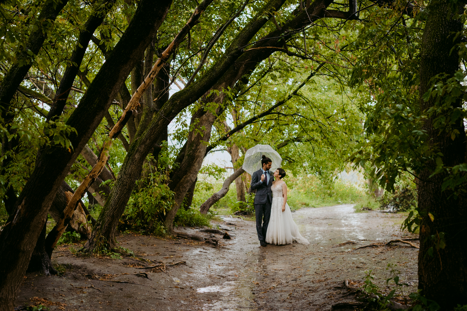 bride and groom standing under tree canopy in the rain