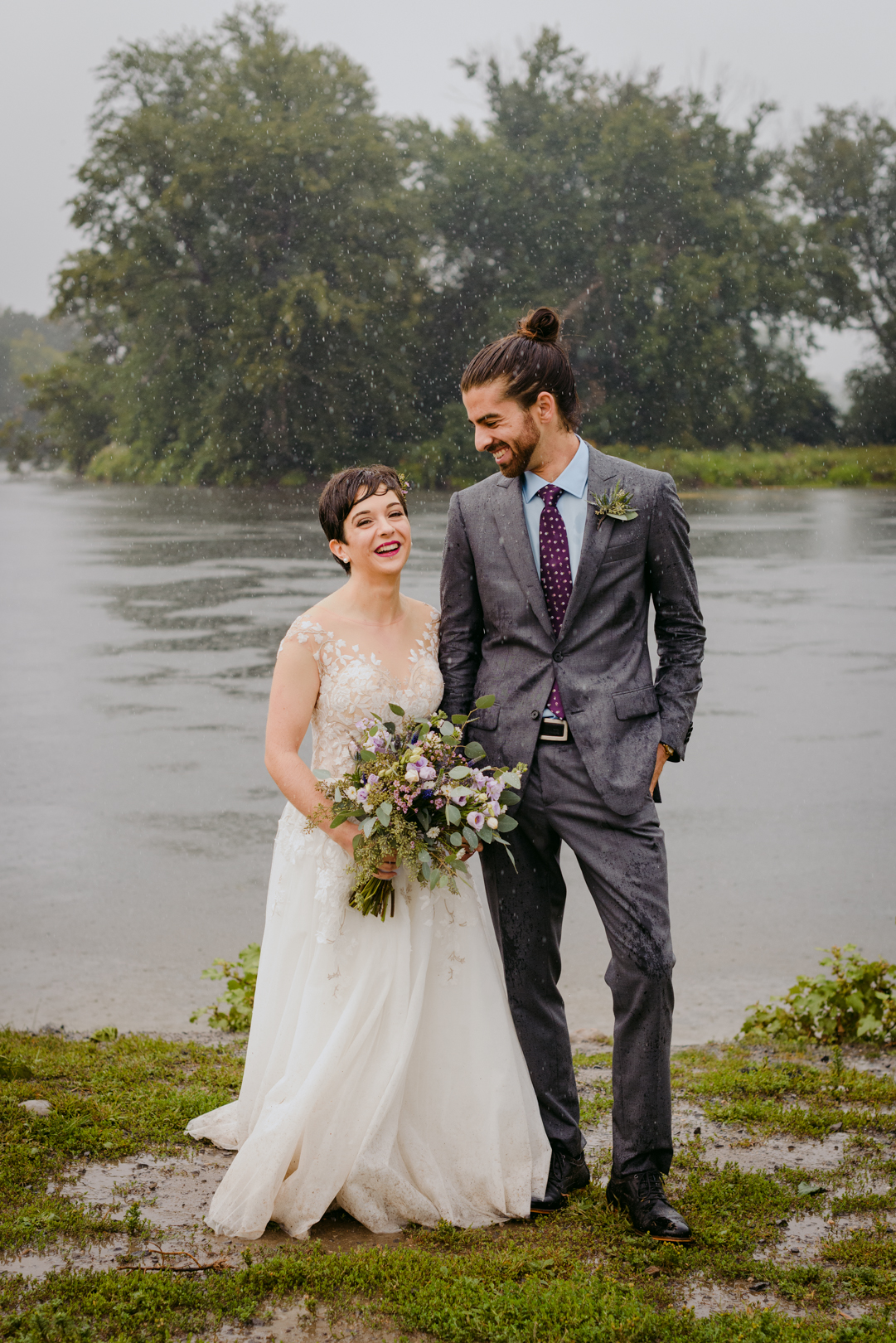 bride and groom standing in the rain by the water soaking wet