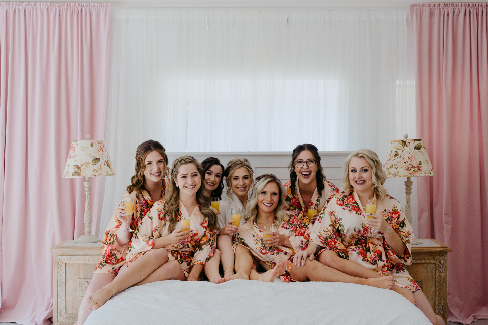 bride and bridesmaids on a bed in floral robes with mimosas