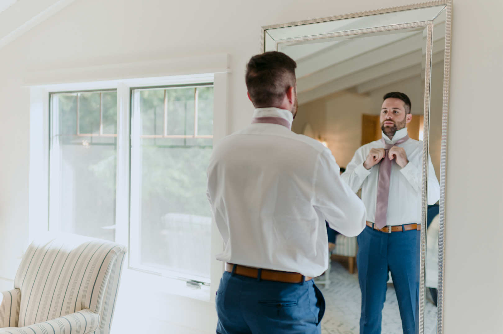 groom tying tie in front of the mirror
