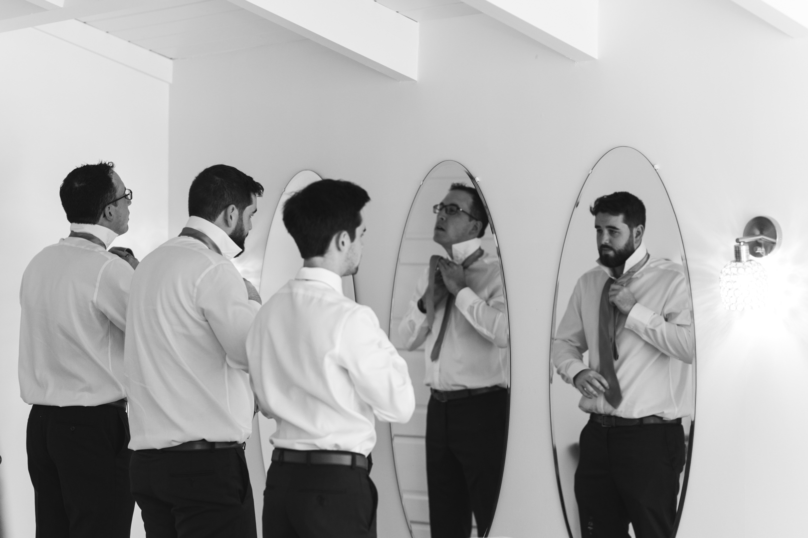groomsmen tying up ties in front of the mirror in black and white