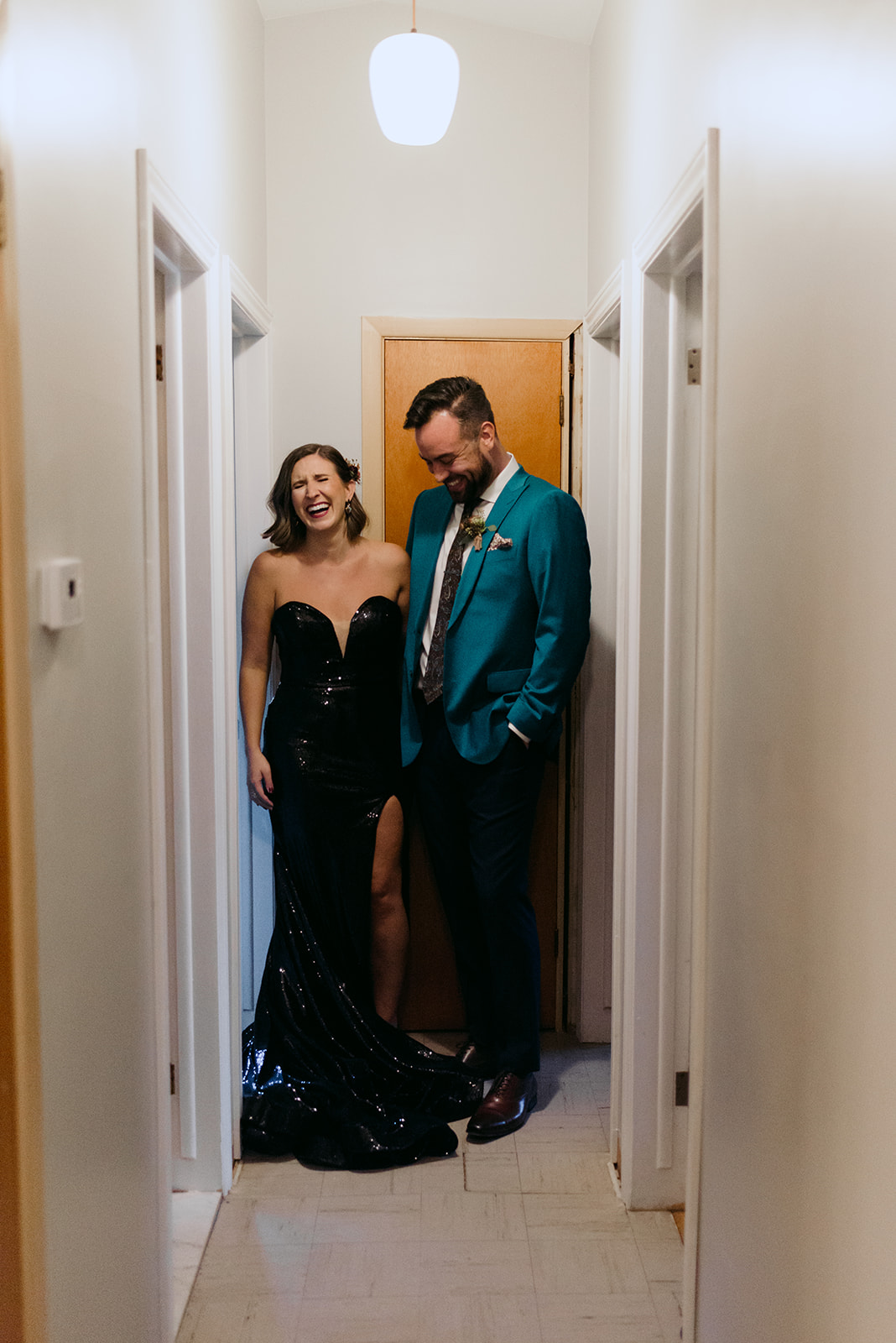 bride in black sequenced dress standing in hallway of their home laughing together