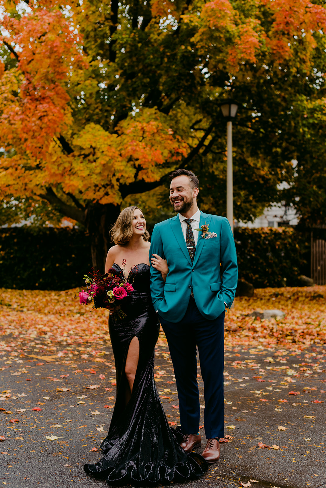 bride in black sequin dress standing with groom outdoors by fall coloured tree