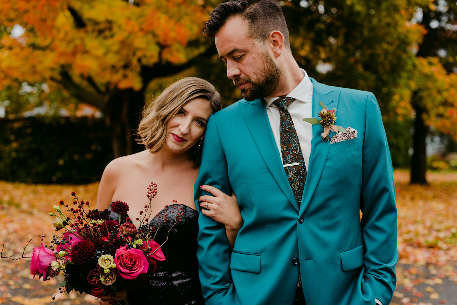 bride in black sequenced dress standing with groom outdoors by fall coloured tree