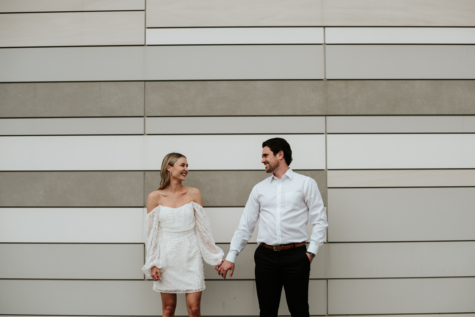 engaged couple holding hands in front of stripe tiled Nordstrom wall