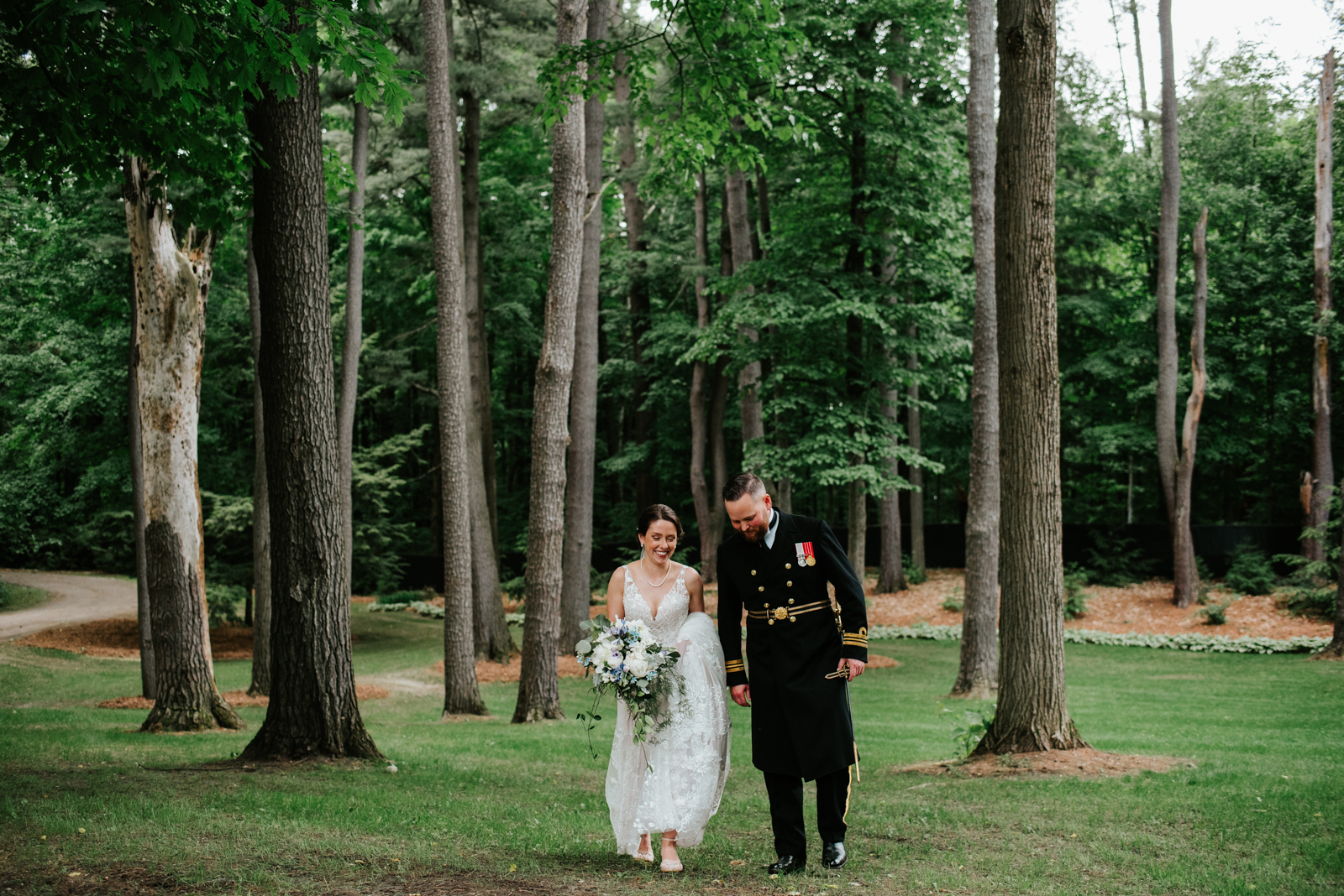 bride and groom wearing canadian navy uniform with sword walking through the trees at outdoor wedding
