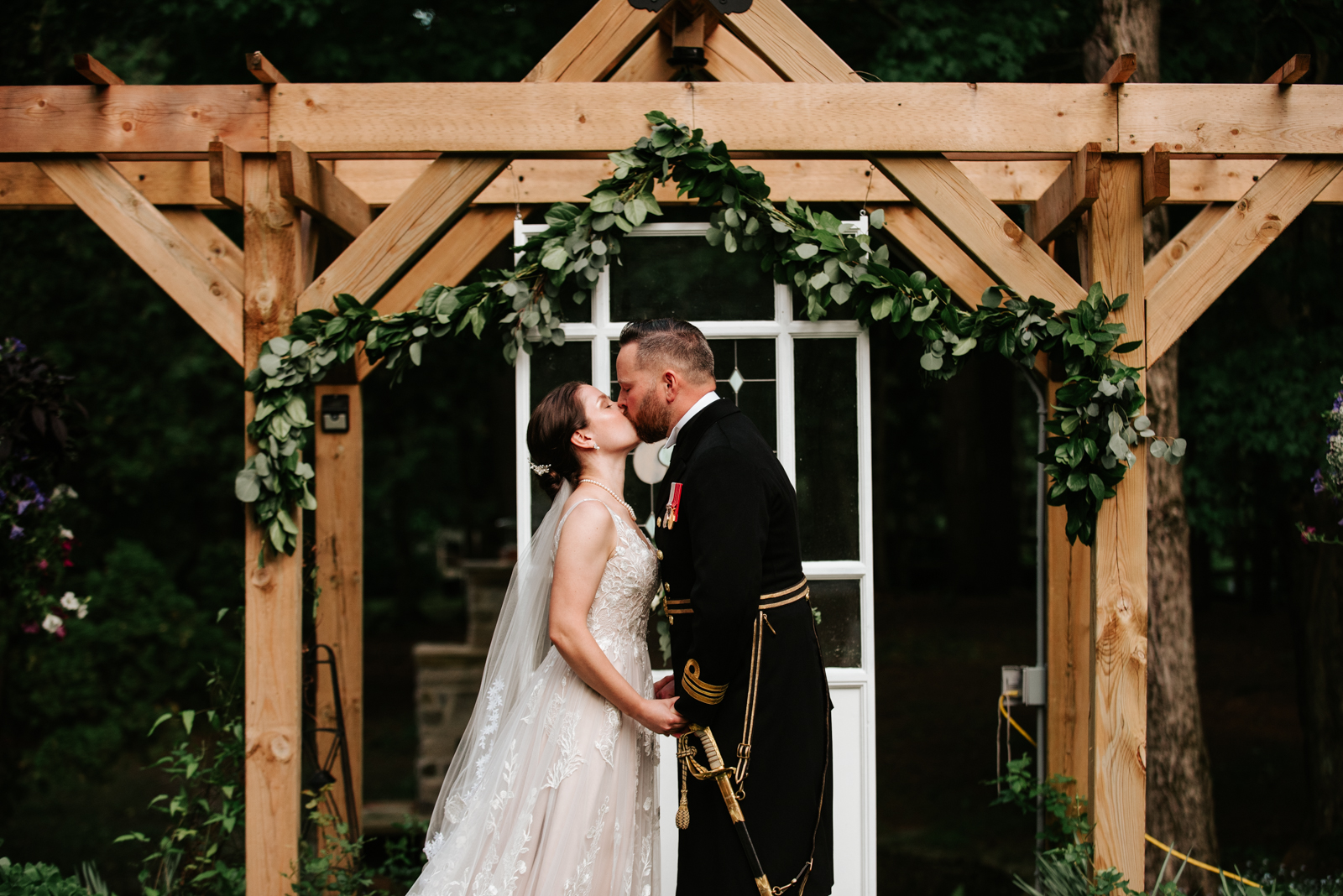 bride and groom in canadian navy uniform with sword first kiss under wooden arbour