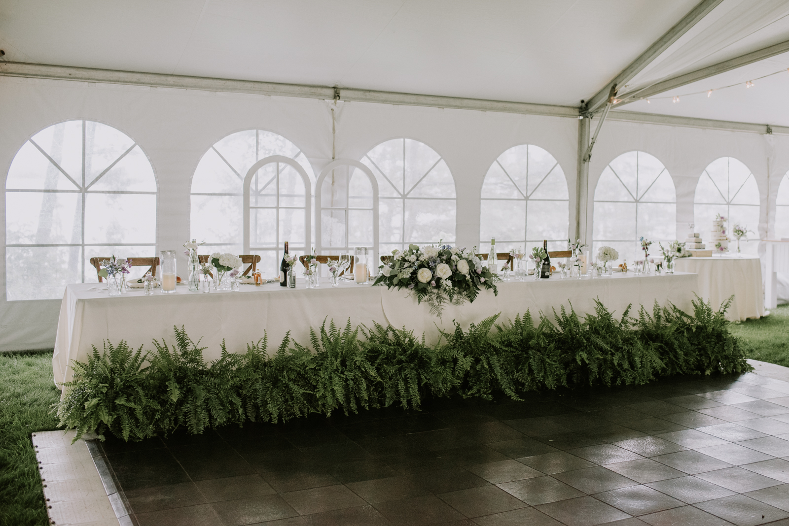 head table with ferns in front under white wedding tent