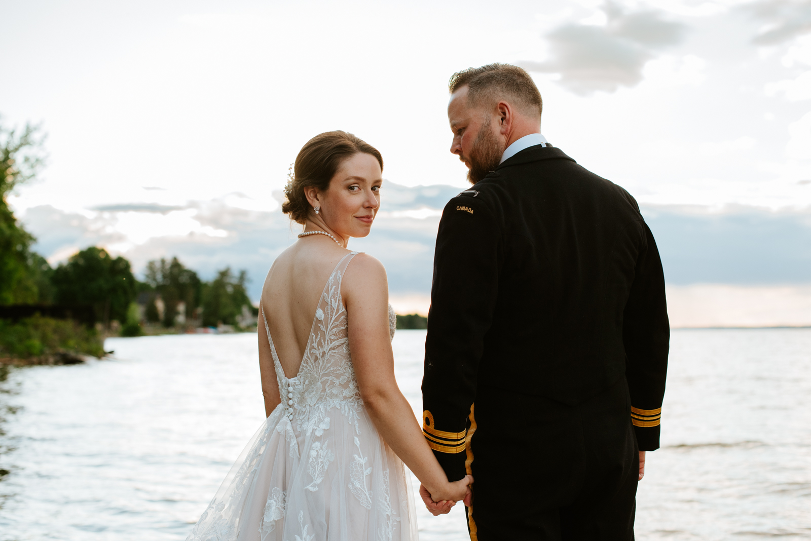 bride and groom wearing navy uniform by the water at sunset