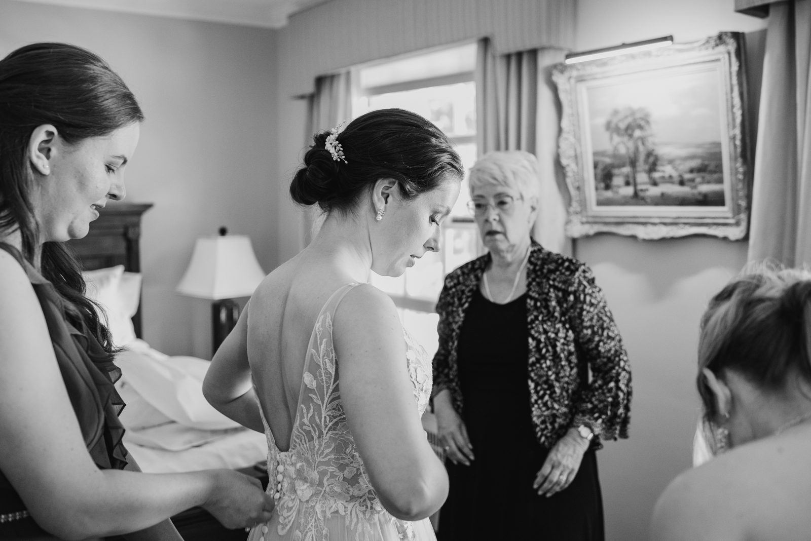 bride putting on her dress with bridesmaids and mother of the bride